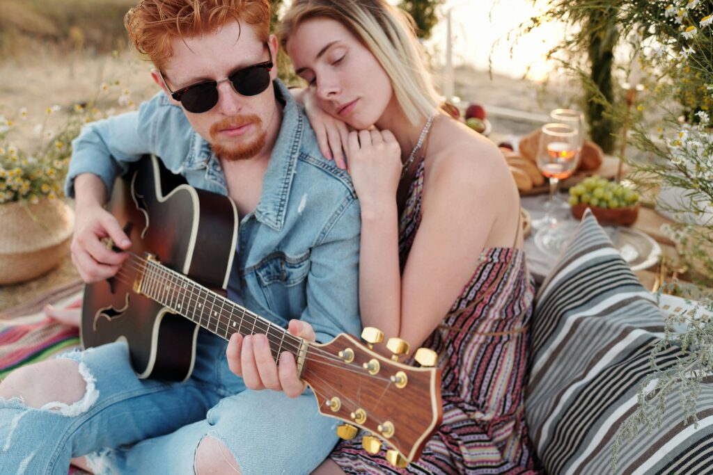 A couple enjoys a romantic picnic outdoors, with music and wine.